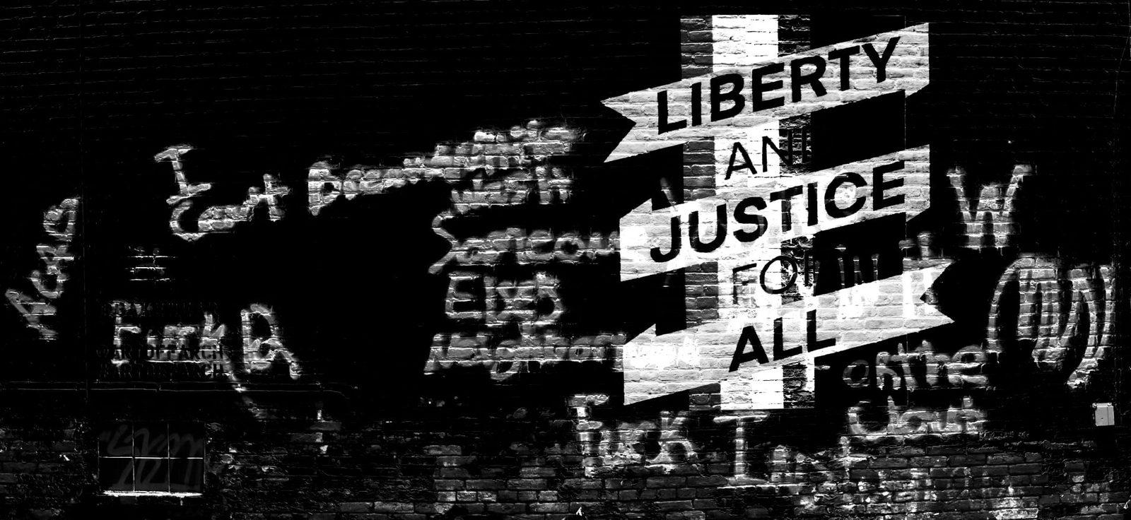 For All — Lancaster. A brick mural — liberty and justice — cut through graffiti. The wall is the record. The camera just stood still.
