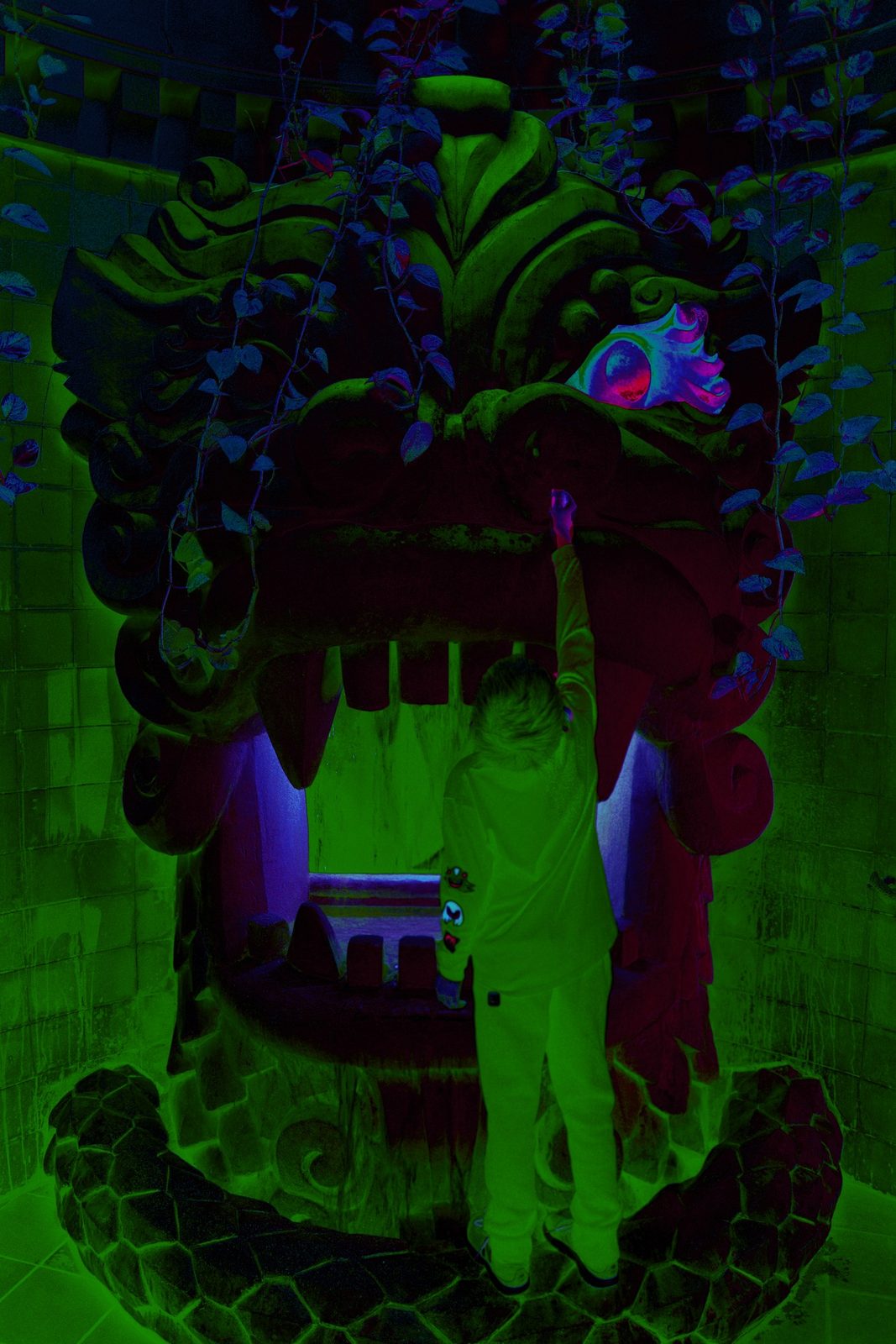 Into the Mouth — Attraction / set. A person reaching into a carved dragon’s mouth under green light. Scale is the joke and the composition.