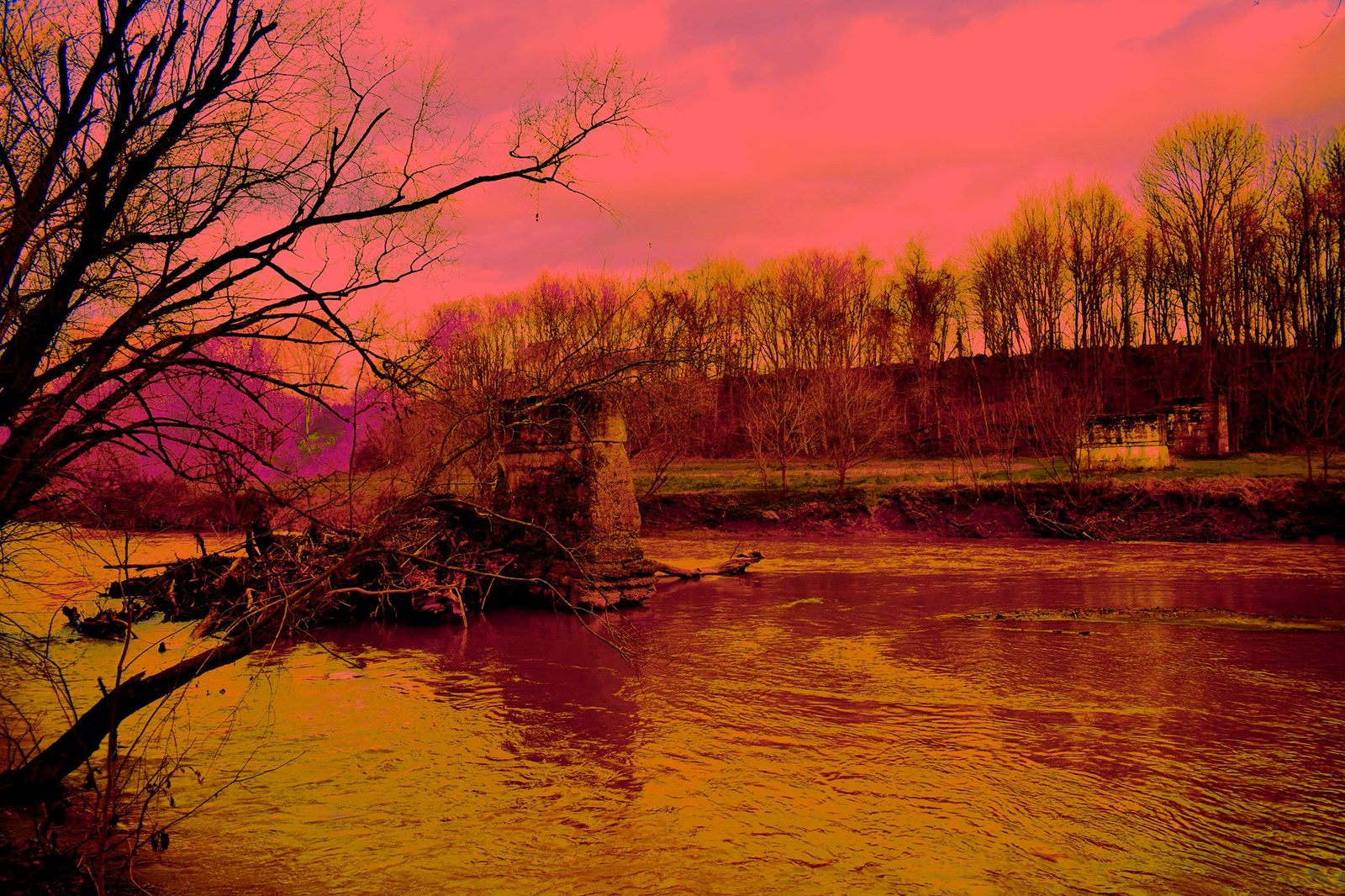 The Pier That Was — Lancaster County. A stone remnant in the current, trees stripped for winter, a red sky. Whatever this pier used to hold, the river kept the footing.