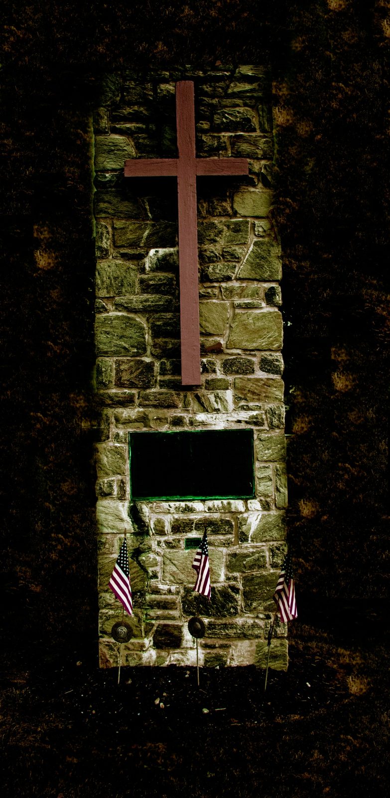 The Wayside Cross — Lancaster County. Stone pillar, wooden cross, three small flags. A roadside memorial shot from above. Quiet, and meant to be.